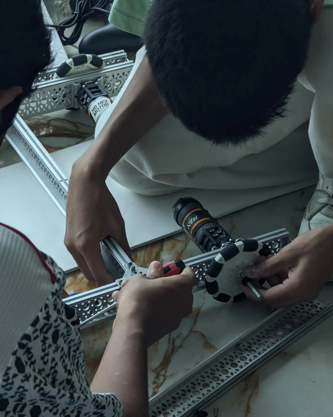 Students assembling an aluminium robotics chassis with motors and brackets on the floor.